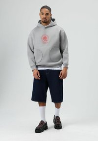 Grijze hoodie met logo-print, twee grote voorzakken, gecombineerd met donkerblauwe denim shorts en zwarte sneakers met roze veters. Witte sportsokken.