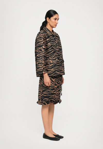 Zwart en oranje outfit met tijgerprint, bestaande uit een losse top en rok, met een kraag en een gerimpelde zoom, gecombineerd met zwarte ballerina's.
