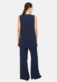 Top senza maniche di colore blu navy con dettaglio a chiave sul retro, abbinato a pantaloni a gamba larga nello stesso materiale, creando un look coeso.