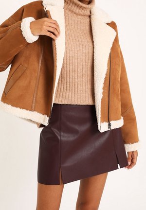 Bruine suède jas met witte sherpa voering, beige geribbelde coltrui en een donker bordeauxleren minirok met een zijsplit.