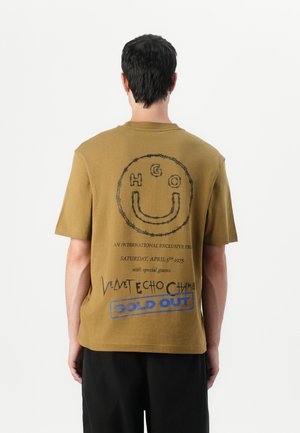 Olivegrünes Baumwoll-T-Shirt mit rundem Ausschnitt, kurzen Ärmeln und einem Grafikdruck mit einem Smiley-Gesicht sowie Veranstaltungsdetails auf der Rückseite.