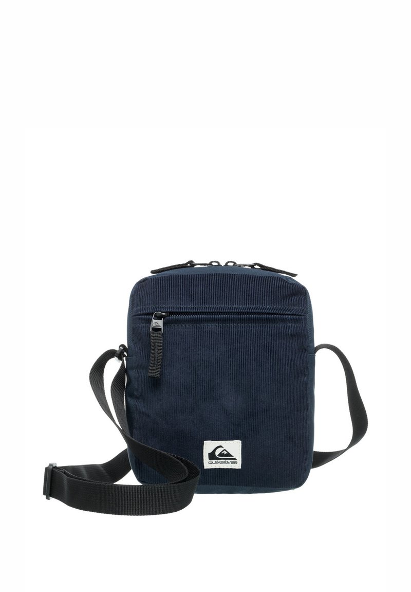 Bolso de hombro de pana color marino con un diseño plano, compartimento principal con cremallera, bolsillo frontal, correa ajustable y una placa con el logo en la parte inferior.