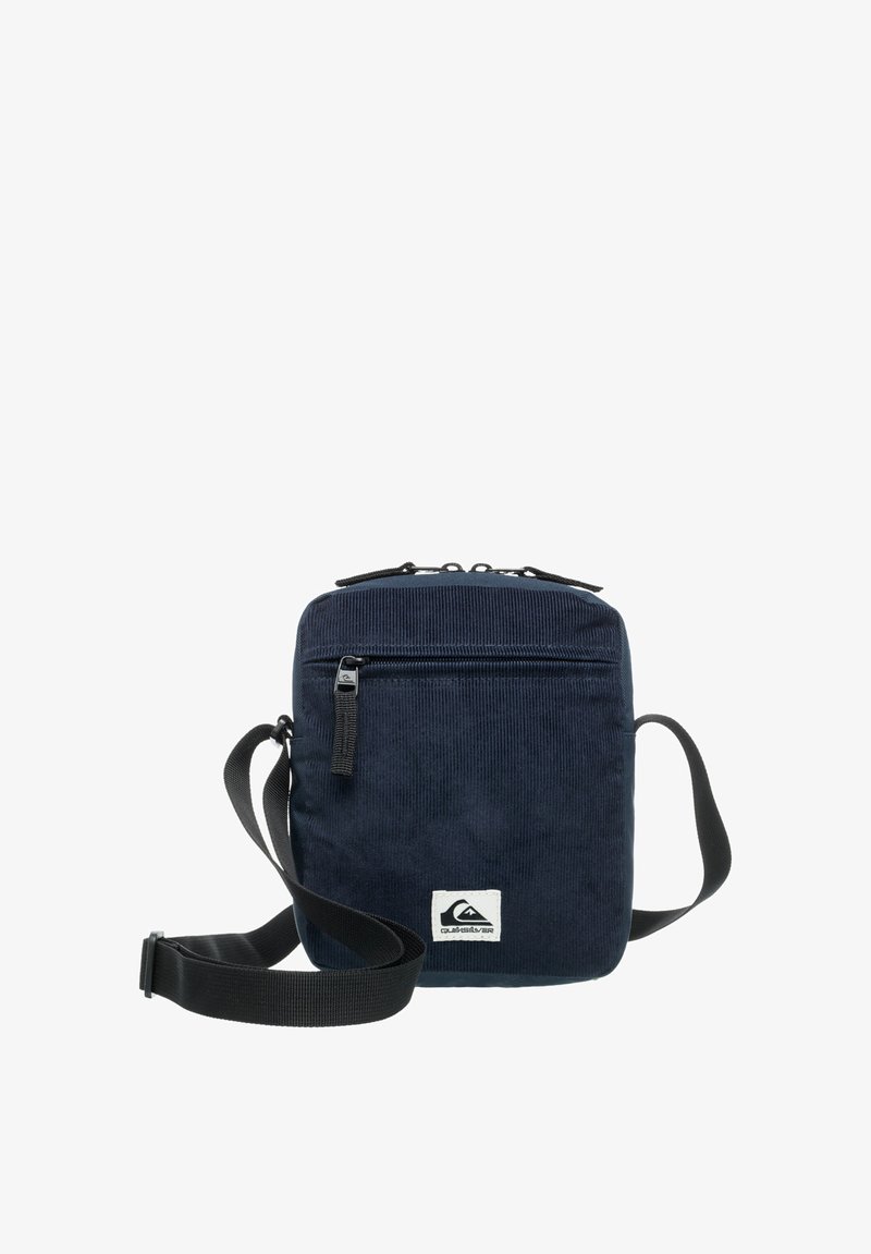 Sac en velours côtelé marine avec un design plat, compartiment principal zippé, poche avant, bandoulière réglable et une étiquette logo en bas.