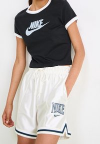 Camiseta negra corta con ribete blanco y logo de Nike; pantalones cortos blancos con detalles en azul, cintura con cordón y logo en la pierna.