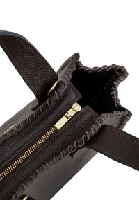 Tumepruun nahast kott nähtava kuldse tõmblukuga ja õmmeldud servadega, avatud, et näha tühja sisemust ja klapiga nupuga kinnitust.