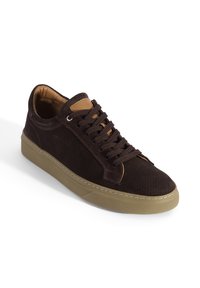 Dunkelbrauner Wildleder-Sneaker mit perforiertem Design, beigefarbenen Lederakzenten, braunen Schnürsenkeln und beiger Gummisohle, vorne rechts schräg auf weißem Hintergrund.