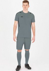Set di abbigliamento sportivo grigio che include una maglietta a maniche corte, pantaloni corti e calze fino al ginocchio. Presenta dettagli neri e il logo del marchio sulla maglietta.