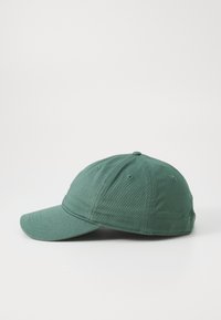 Grønn bomull baseballcap med en buet skjerm, seks ventilasjonsøyler og en stoffjusterbar stropp på baksiden.