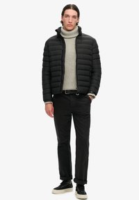 Sort dunjakke med quiltet design, grå turtleneck sweater, sorte bukser og sorte sneakers med hvide såler; ingen synlige logoer.
