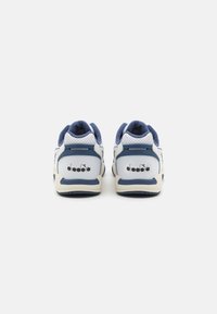 Sneaker da uomo con un design prevalentemente bianco e navy, dettagli in suede, perforazioni decorative e un logo sul retro.