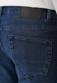 Tamno plavi traperice s stražnjim džepom, s crnom kožnom etiketom s natpisom "ONLY & SONS." Glatka tekstura i klasičan dizajn.