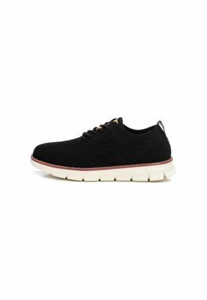 Zapatilla deportiva negra de punto con suela blanca, que presenta un upper texturizado y un sutil acento de una franja roja en el borde de la suela.