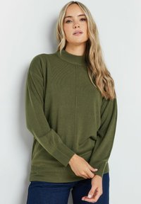 Maglione verde a maglia con collo alto, spalle cadenti e polsini a costine. Presenta una texture liscia e una vestibilità rilassata.