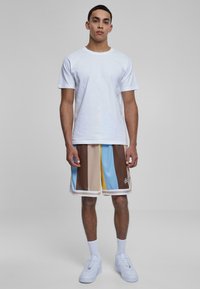 Bela bomba majica in večbarvne kratke hlače z modrimi, rjavimi in rumenimi navpičnimi črtami. Bele športne čevlje z teksturiranimi podplati.