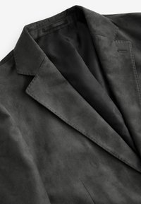 Dunkelgrauer Blazer mit einer weichen, suedartigen Textur. Besitzt einen Reverskragen, dezente Nähte und ein schwarzes Satinfutter.