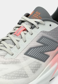 Gray athletic shoe with a textured design, featuring gray and pink accents, reflective details, and a cushioned sole. 2025 New York Marathon branding.