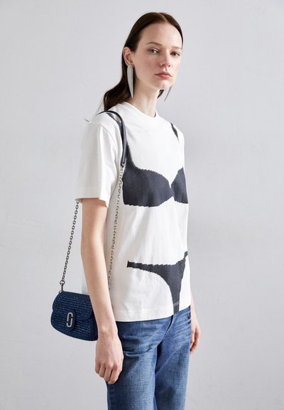 White cotton t-shirt featuring black graphic of a bra and panties, paired with blue denim jeans and a small blue woven handbag.