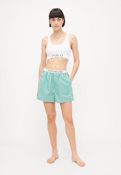 Balts īsais tops ar "POLO" logotipu, kas savienots ar zaļām un baltām svītrainām šortiem ar elastīgu jostasvietu, uz kuras rakstīts "POLO RALPH LAUREN".