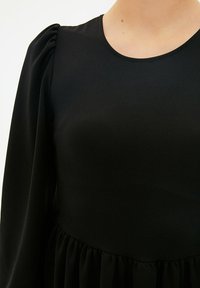 Czarna sukienka z okrągłym dekoltem, bufkowymi rękawami i marszczoną talią. Materiał jest gładki o subtelnej teksturze.