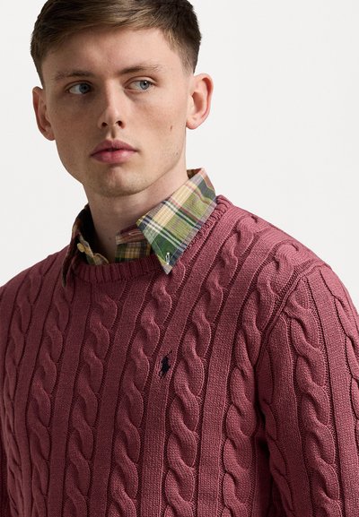 Cable-knit sweater in dark pink with a crew neck and small logo; paired with a green and purple plaid shirt underneath.