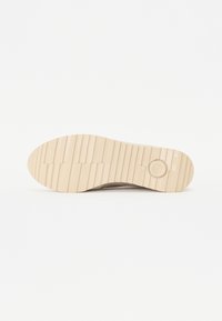 Semelle de chaussure beige clair avec des rainures horizontales et un dessin circulaire près du talon sur un fond blanc uni.