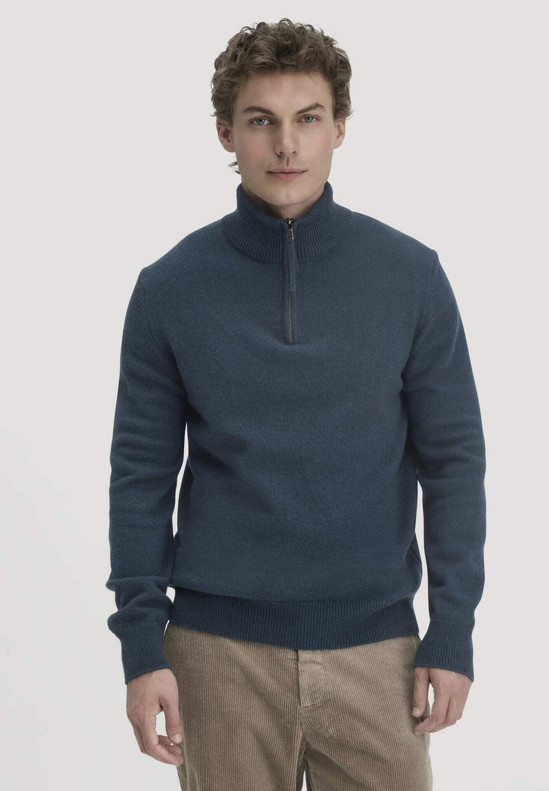 Dunkelblauer Pullover mit Reißverschluss aus strukturiertem Strick, ausgestattet mit gerippten Bündchen und Saum, kombiniert mit beigen Cordhosen.