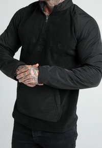 Pullover in fleece nero con design a mezza zip, caratterizzato da maniche lisce nere a contrasto e un logo ricamato sul petto.