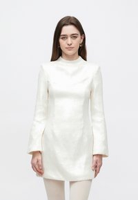 Witte mini-jurk met lange wijde mouwen, gestructureerd silhouet, textuurrijke glans en een hoge hals. De stof lijkt ingewikkeld en reflecterend.