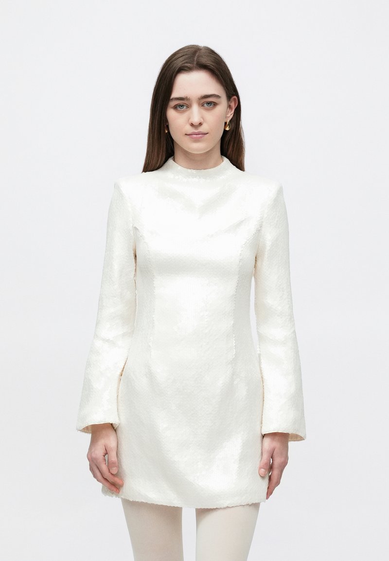 Witte mini-jurk met lange wijde mouwen, gestructureerd silhouet, textuurrijke glans en een hoge hals. De stof lijkt ingewikkeld en reflecterend.