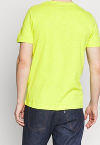 Triko s krátkým rukávem a kulatým výstřihem v jasné neonově žluté barvě, vyrobené z měkké, texturované látky. Má standardní střih a rovný lem na zadní straně.