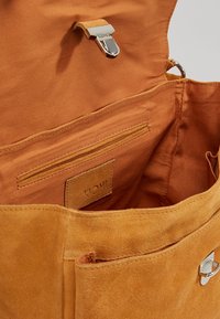 Intérieur de sac en daim marron avec une texture lisse. Comprend une poche zippée, une poche fendue et une fermeture à boucle en métal argenté.