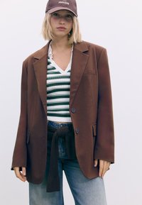 Brun blazer med to knapper, båret over en stribet top i grøn og hvid samt højtaljede denim, med et knyttet brunt slips.