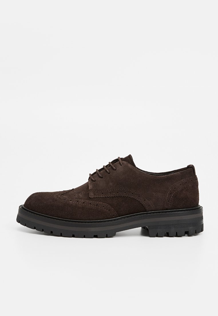 Ciemnobrązowe zamszowe męskie buty typu brogue z zapięciem na sznurowadła i grubą czarną gumową podeszwą, widok z boku na białym tle.