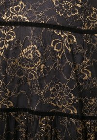 Black lace fabric featuring gold floral patterns, with a textured surface. Black velvet trim accentuating the ruffled design.