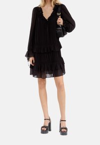 Vestido negro con volantes, de manga larga, escote en V y diseño en capas. Combinado con sandalias de plataforma negras con detalle de lazo y tachuelas.