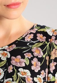 Tejido negro con un patrón floral; presenta flores rosa y blancas con hojas verdes. Cuello redondo, textura suave y ajuste estructurado.