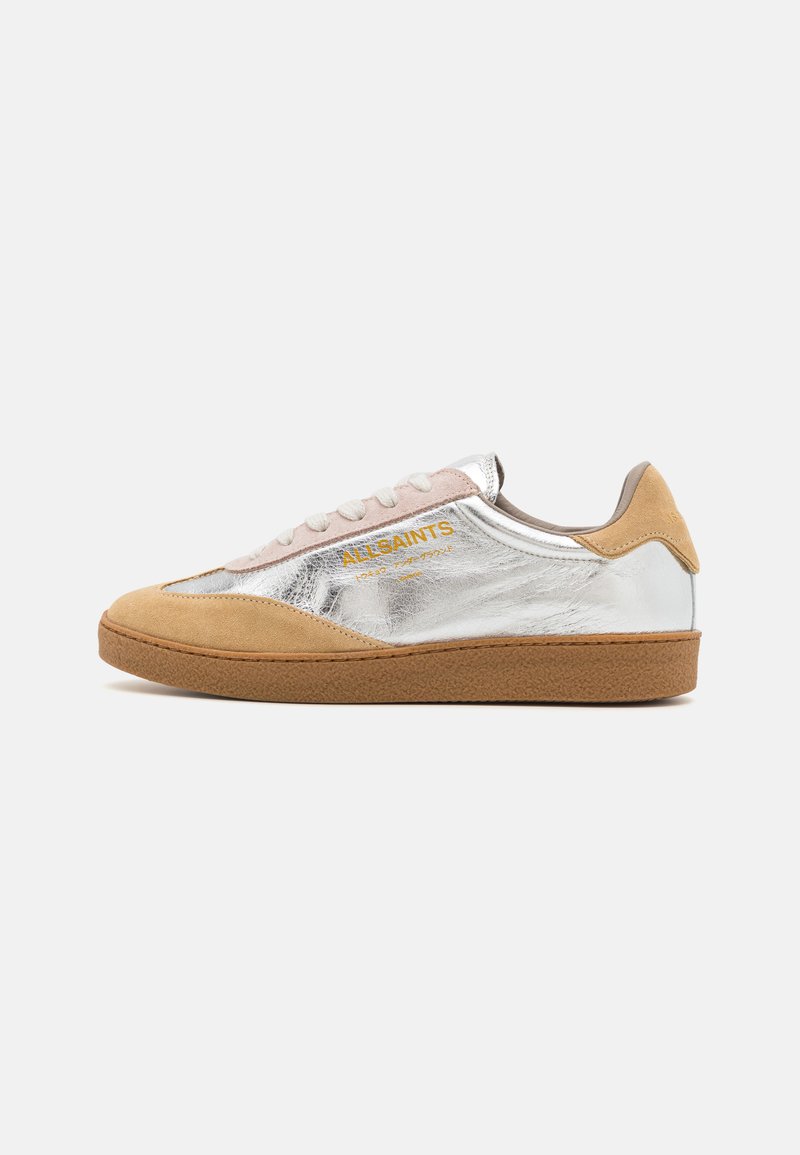 Zapatillas de ante plateadas y beige con suela de goma textura, cordones beige y un logotipo impreso en amarillo en el lateral.