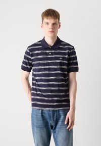 Mørkeblå polo skjorte med horisontale hvite striper, to knapper ved kragen og en liten logo på venstre bryst. Ledig passform.