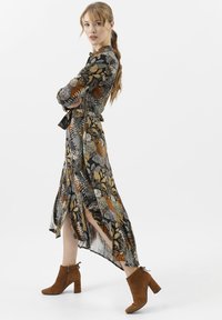 Abito lungo e decorato con motivi floreali nei colori nero, oro e arancione. Abbinato a stivaletti alla caviglia in suede marrone con tacco spesso.