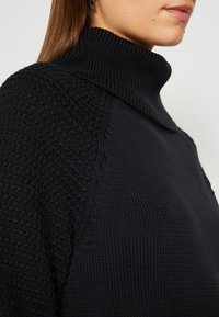 Schwarzer gestrickter Rollkragensweater aus strukturiertem Stoff, mit geripptem Kragen und Nähten, der eine moderne, lässige Silhouette präsentiert.