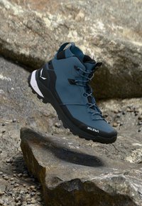 Botte de randonnée bleu foncé avec une tige texturée, un système de laçage et des accents noirs. Présente une semelle robuste et un détail de marque sur le côté.