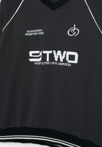 Črna majica z v-izrezom in belim trakom, na sprednji strani prikazuje besedilo "E.S.M4046264 REGISTER CODE", logotip in "9TWO ADAPTATIVE LOCAL SERVICES".