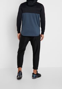 Sort og mørkeblå hættetrøje med lange ærmer, der har et farveblokerende design. Kombineret med sorte tapered bukser og sportssko.