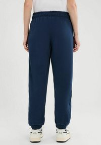 Granatowe dresy z elastycznym pasem i mankietami. Wykonane z miękkiego materiału, o luźnym kroju. Noszone z białymi trampkami.