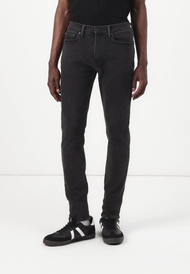 Vaqueros slim-fit negros con cinco bolsillos, denim de peso medio y un sutil desvanecimiento. Combinados con unas zapatillas en blanco y negro que cuentan con una parte superior texturizada.