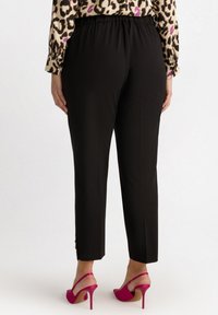 Pantaloni neri a sigaretta con vita elastica, caratterizzati da una texture liscia e dettagli decorativi con bottoni all'orlo, abbinati a scarpe con tacco rosa.