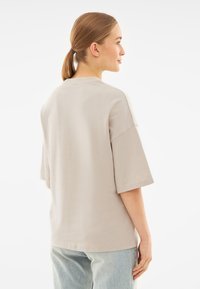 Tricou din bumbac oversize bej, cu umeri căzuți și mâneci scurte. Textură netedă, decolteu rotund și tiv drept.