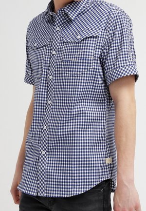 Camicia a maniche corte con bottoni in colore blu navy e motivo a quadretti bianchi, dotata di due tasche sul petto e un orlo curvato.