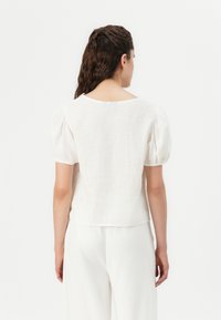 Hvit linbluse med pufferm, rund hals og avslappet passform. Har en jevn tekstur og enkelt design.