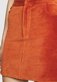 Jupe en velours côtelé orange à surface texturée, dotée de poches latérales et de coutures visibles le long des coutures.